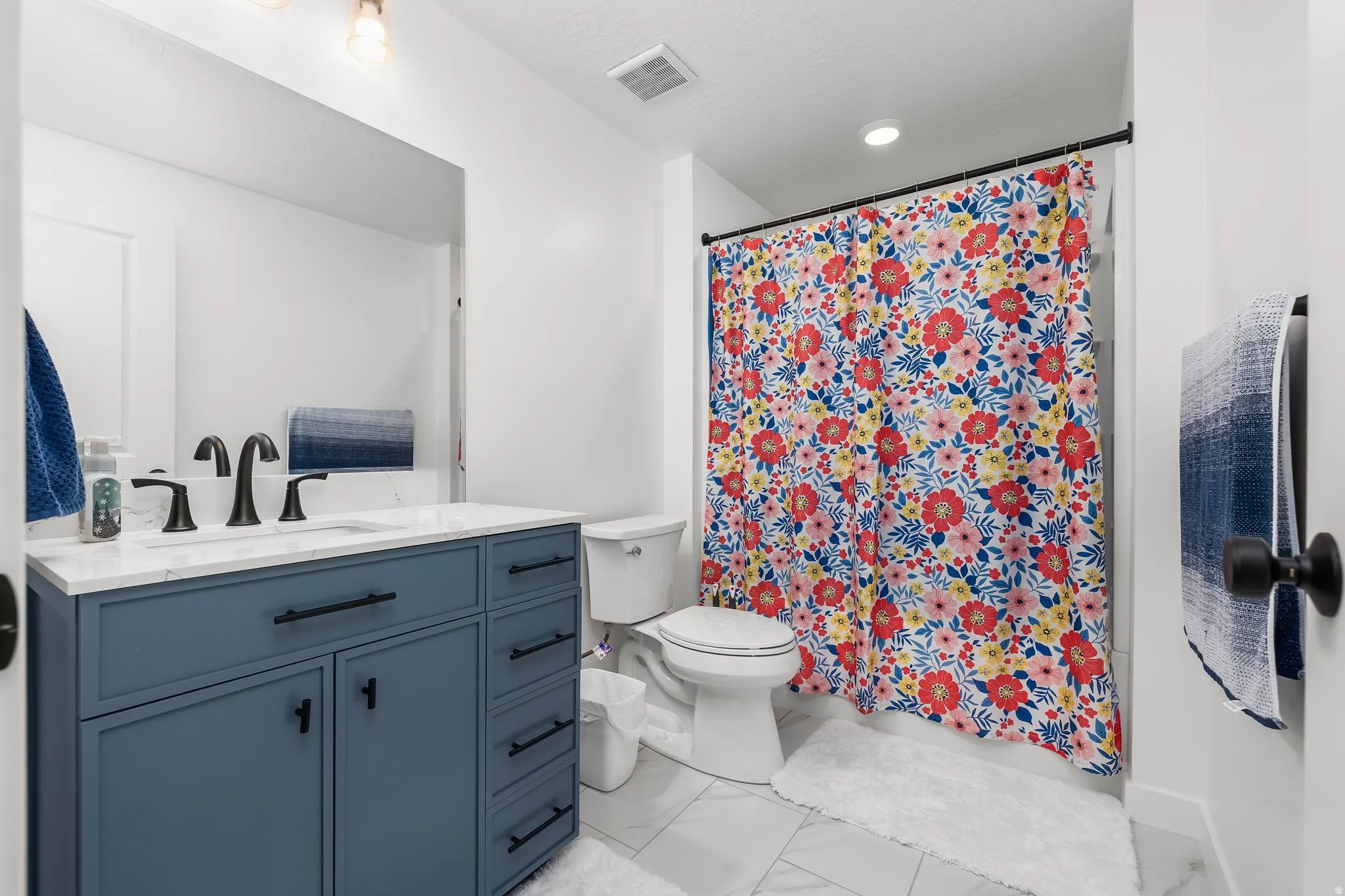 Bathroom featuring a blue vanity with a white countertop, matte black fixtures, a built-in mirror, and tile flooring