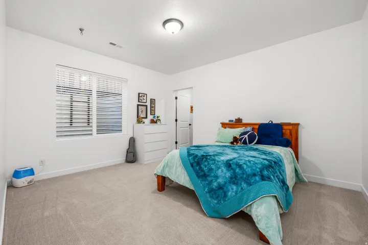 Bedroom featuring a rectangular window with horizontal blinds, neutral-toned carpet flooring, white painted walls, a flush-mount ceiling light fixture, and a white baseboard trim