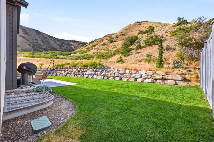 Expansive backyard featuring a lush lawn, concrete patio, and a stone retaining wall