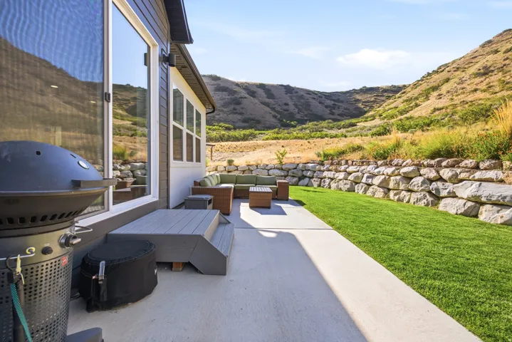 Expansive outdoor patio featuring concrete paving, a green lawn, and a stone retaining wall