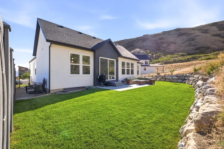 Expansive backyard featuring a manicured lawn, a large concrete patio, and a natural rock retaining wall