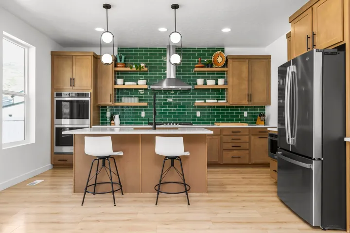Modern kitchen featuring a bold green subway tile backsplash, light wood-finish flooring, and light-toned cabinetry