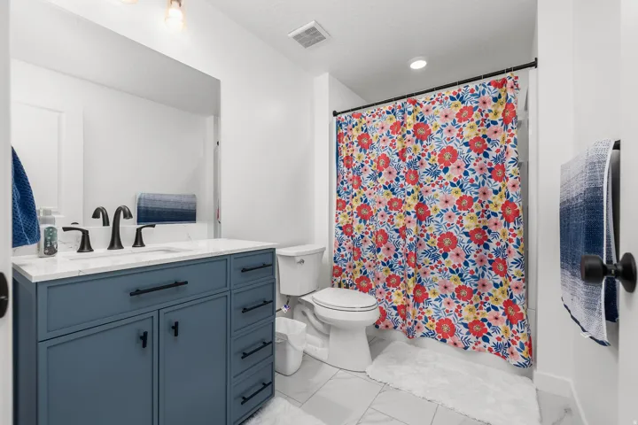 Bathroom featuring a blue vanity with a white countertop, matte black fixtures, a built-in mirror, and tile flooring