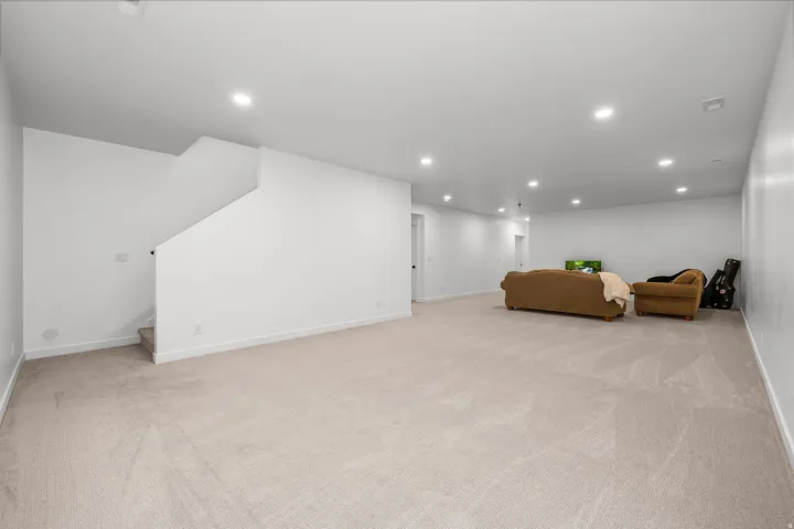 Expansive carpeted room featuring recessed lighting and a staircase with a half-wall railing
