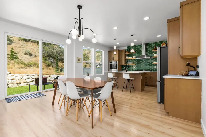 Open-concept living space featuring wood-finish flooring, a modern linear chandelier, and a kitchen with a green subway tile backsplash
