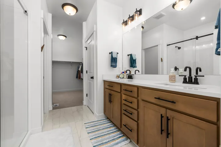 Bathroom featuring a double vanity with light wood-finish cabinetry, white countertop, and black fixtures