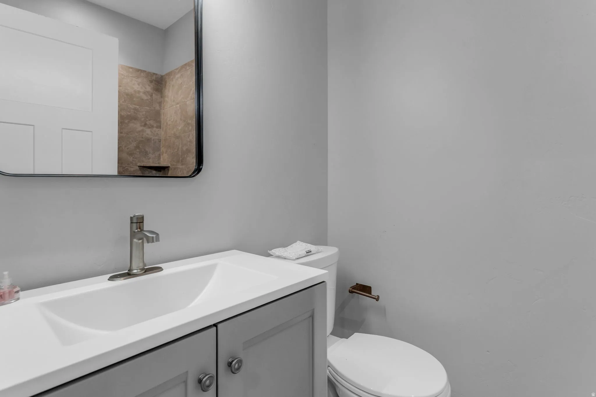 Bathroom featuring a gray vanity with a white countertop, a white sink with a brushed nickel faucet, and a wall-mounted mirror