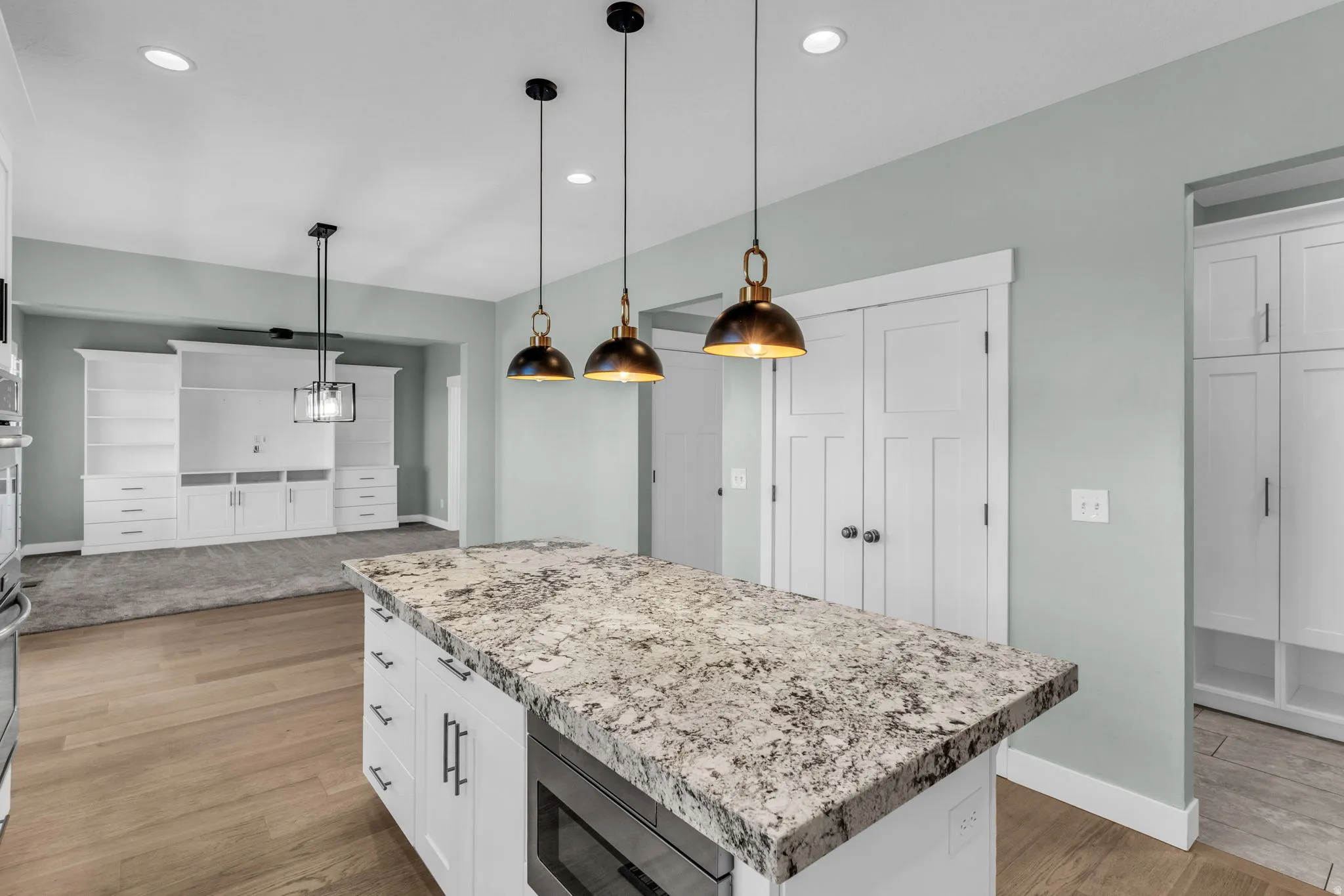 Kitchen island featuring a substantial stone countertop, integrated microwave, and pendant lighting