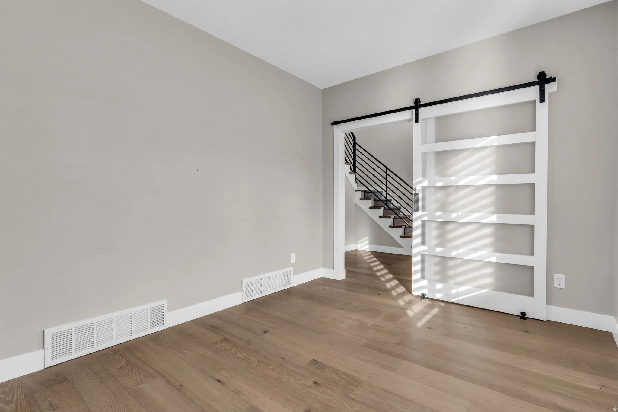 Spacious room featuring wood-finish flooring and a contemporary barn door with black hardware