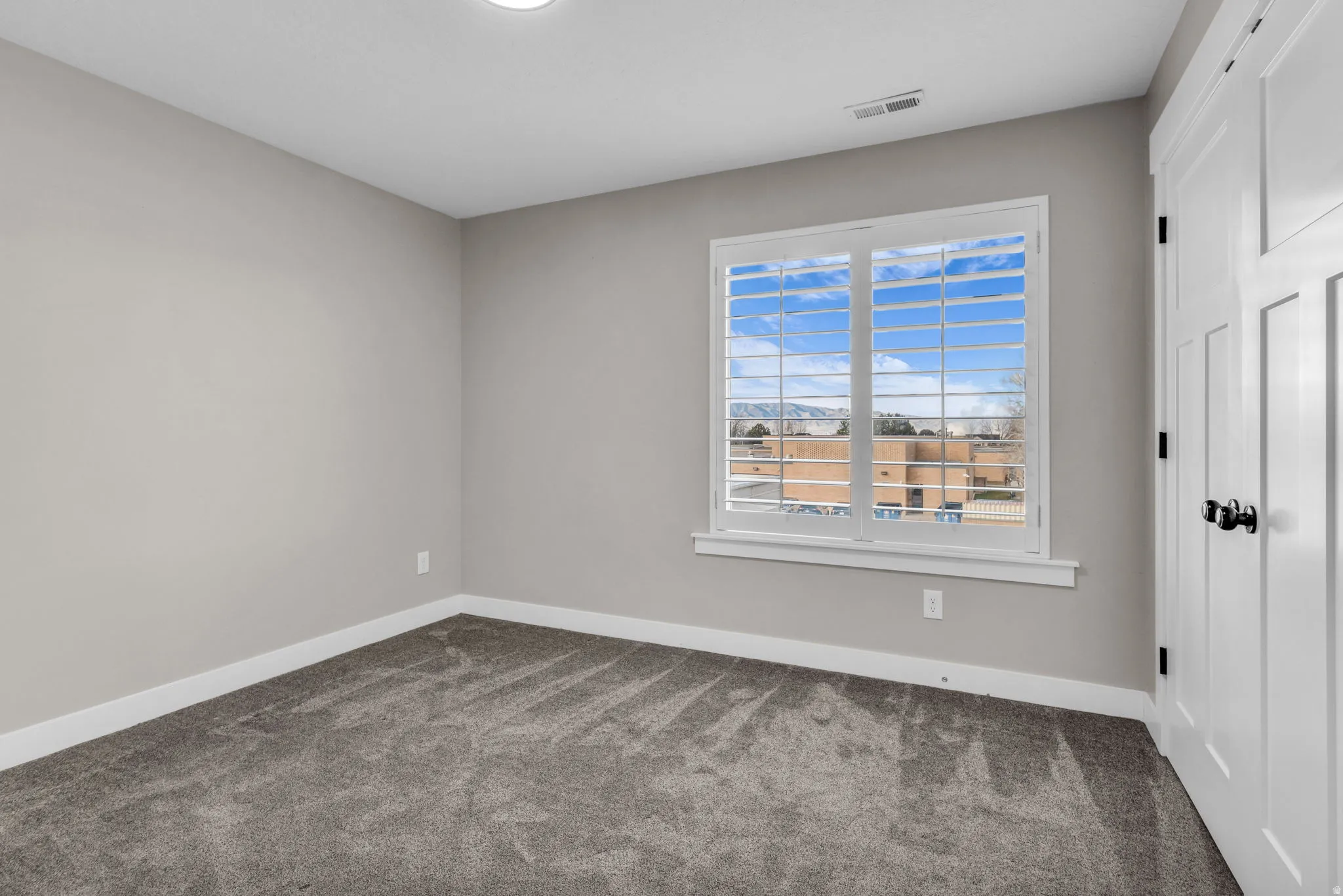 Spacious room featuring neutral paint, gray carpet flooring, white baseboards, and a window with plantation shutters