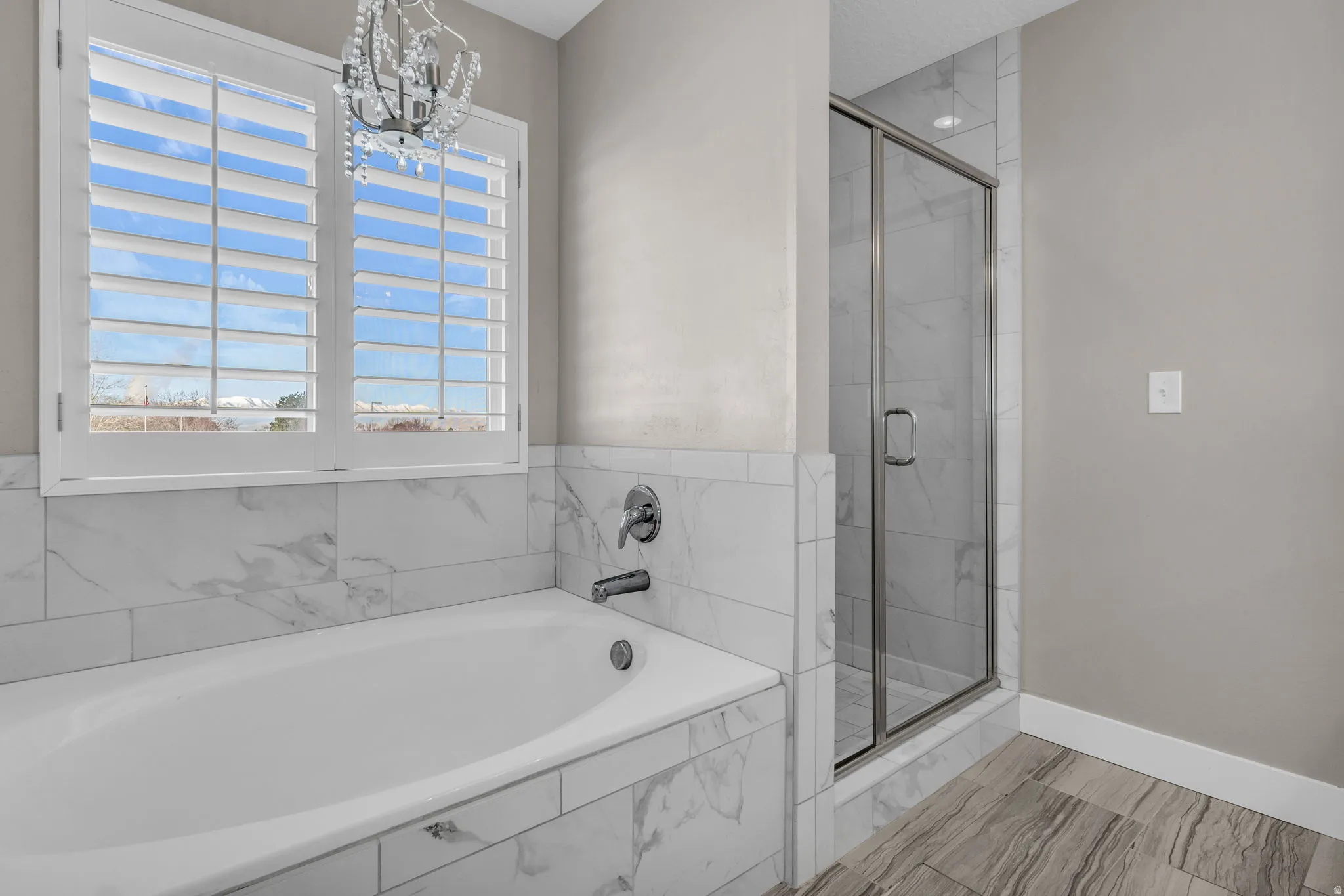 Soaking tub with surrounding marble-look tile, complementing a glass-enclosed shower with matching tile
