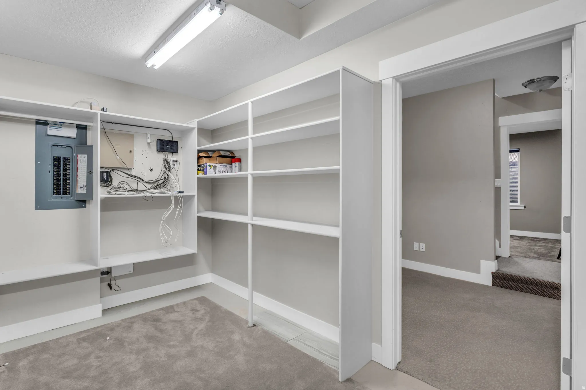 Storage room featuring built-in shelving, a dedicated electrical panel, and a utility shelf