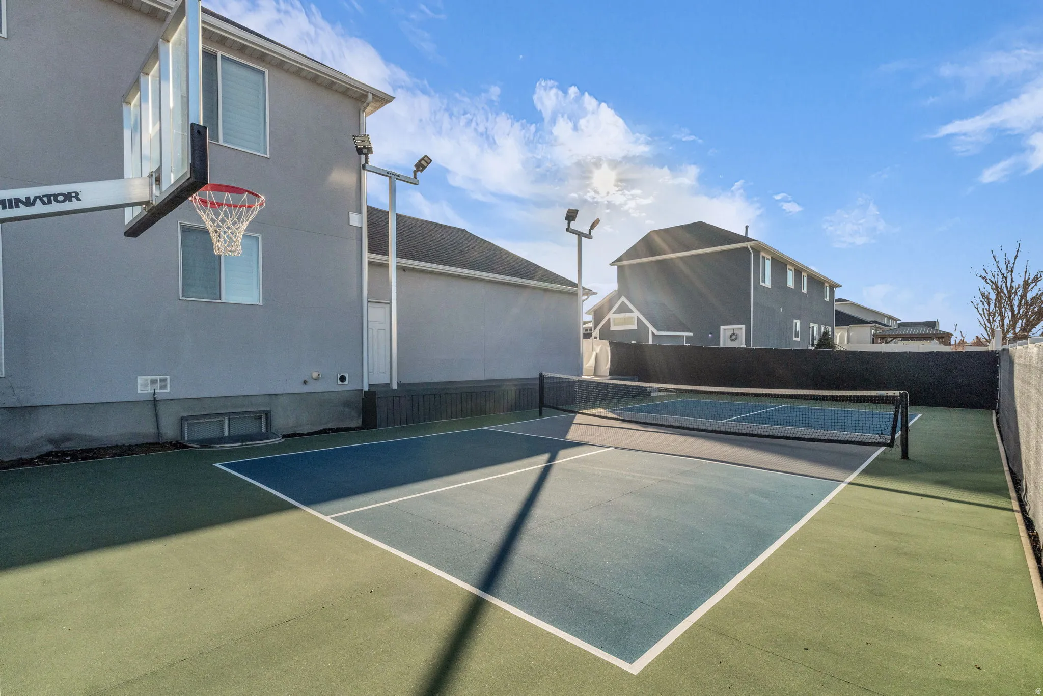Sport court featuring a pickleball court with net, basketball hoop, and perimeter fencing