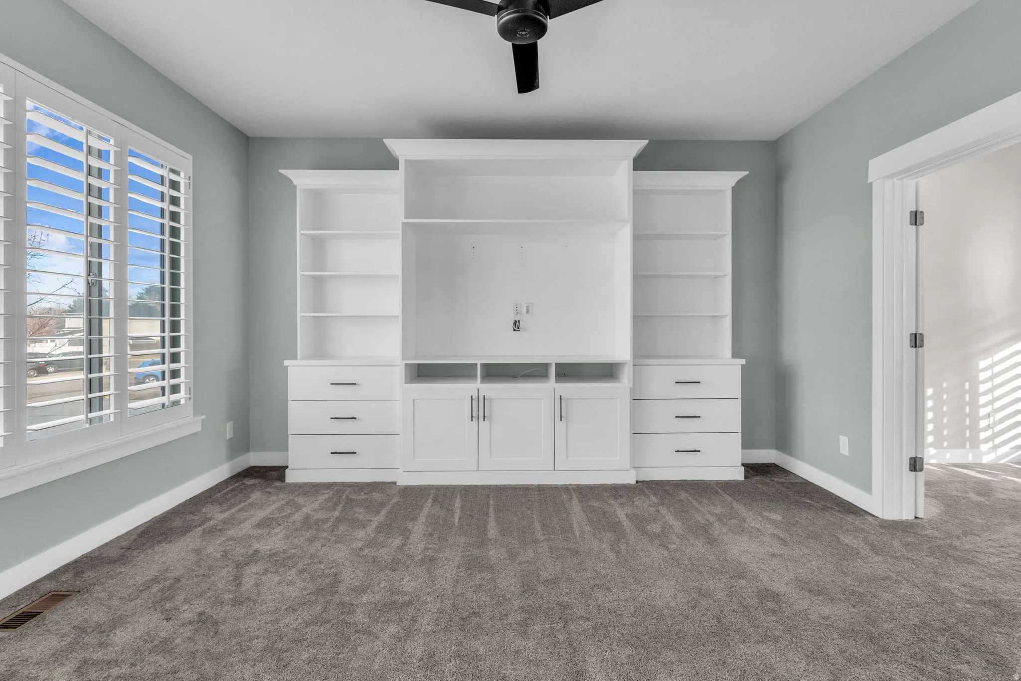 Built-in media center with shelving and cabinet storage, complemented by a large window with white plantation shutters