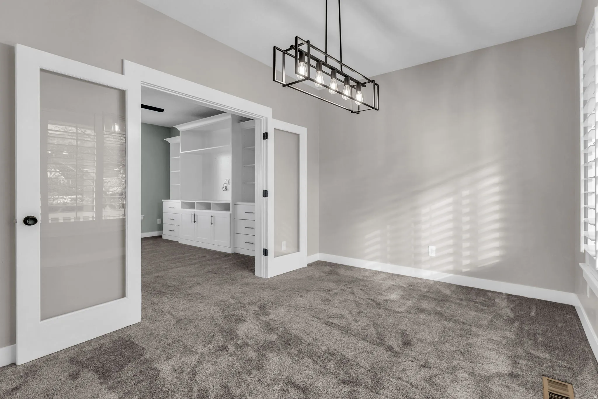 Double glass-paneled doors opening to a room featuring extensive built-in white cabinetry with shelving