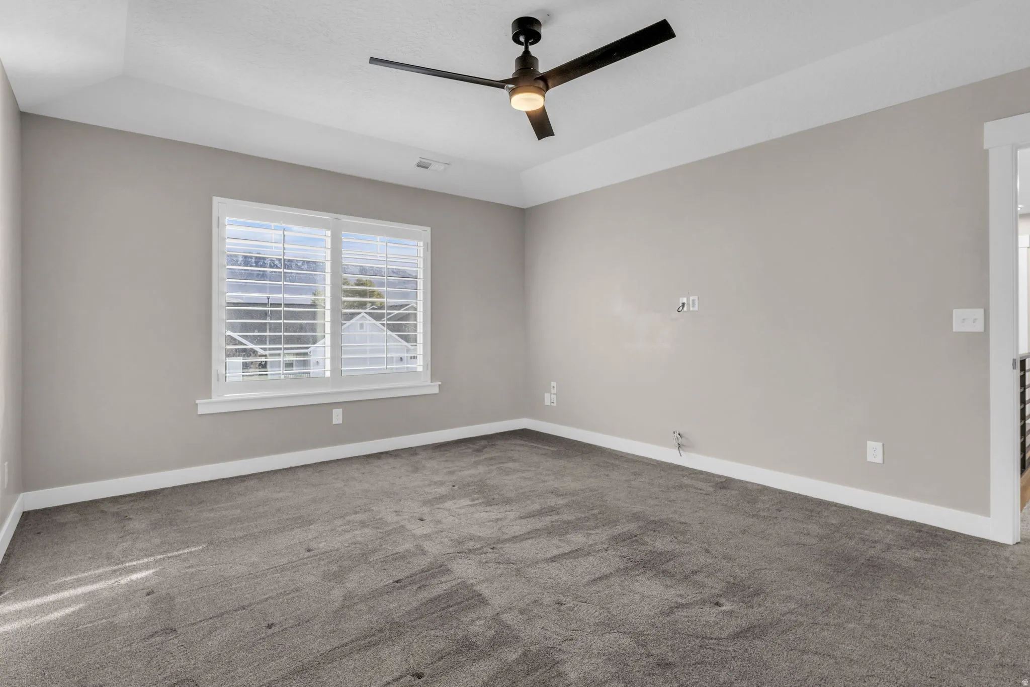 Spacious room featuring neutral carpeting, light gray walls, a tray ceiling, and a contemporary ceiling fan