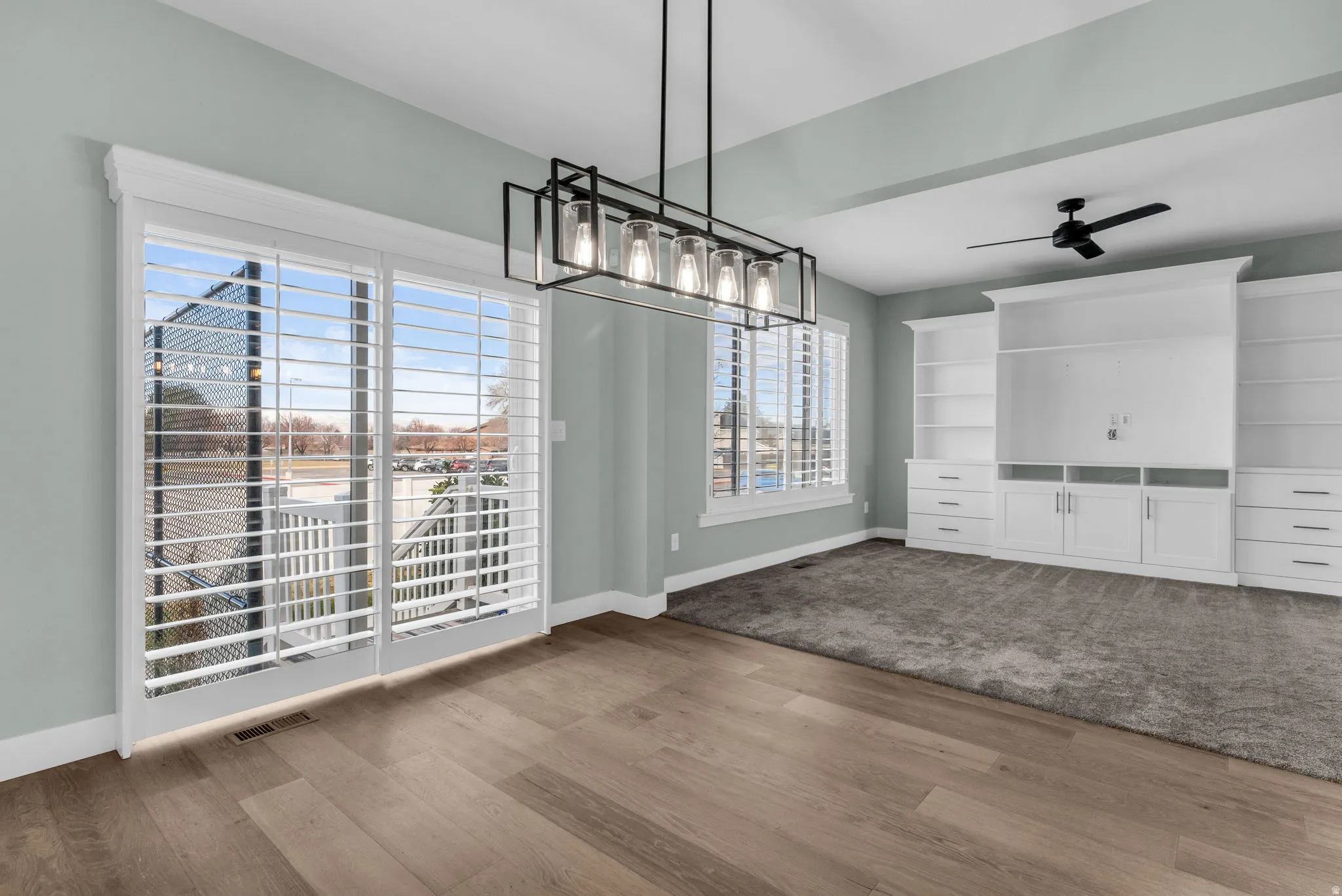 Spacious room featuring wood-finish flooring, a contemporary linear chandelier, and sliding glass doors with plantation shutters