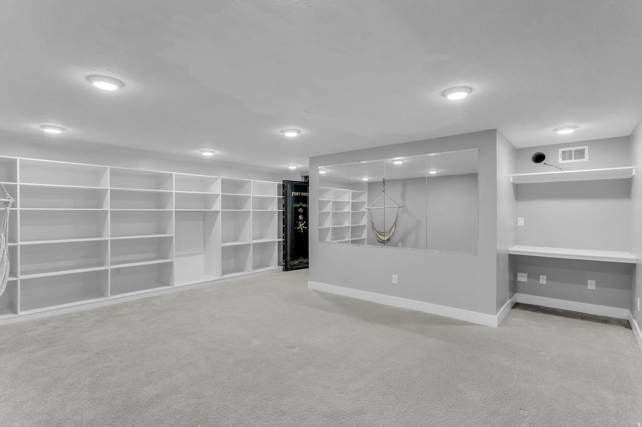 Spacious room featuring extensive built-in shelving, recessed ceiling lighting, light gray carpeting, and a built-in desk area with shelving