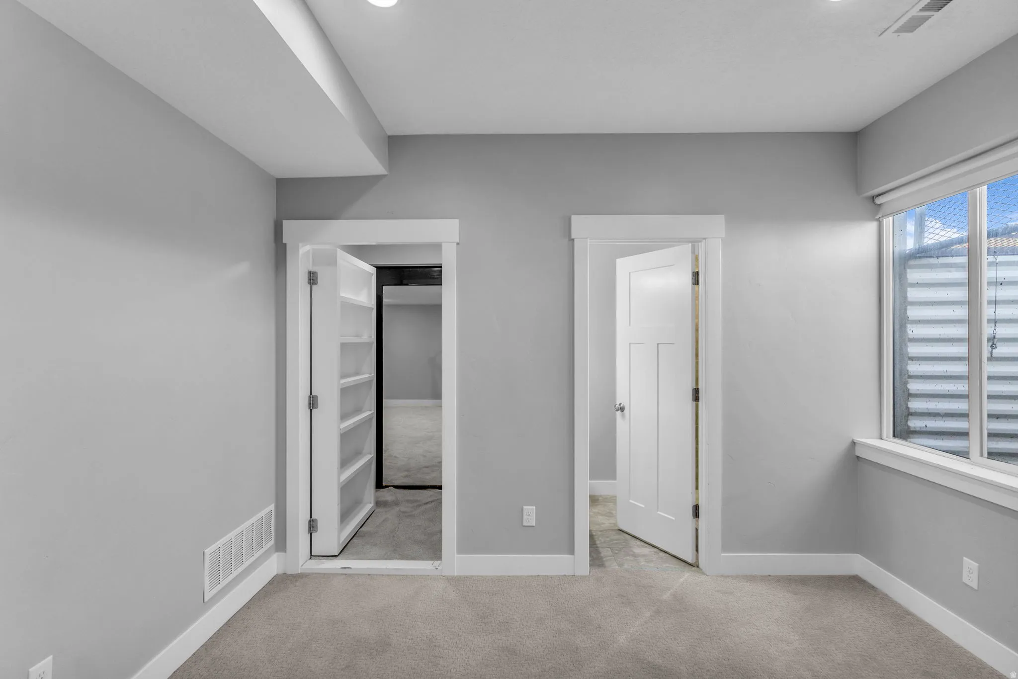 Carpeted room featuring a white paneled door, a window with a white frame, and a built-in shelving unit