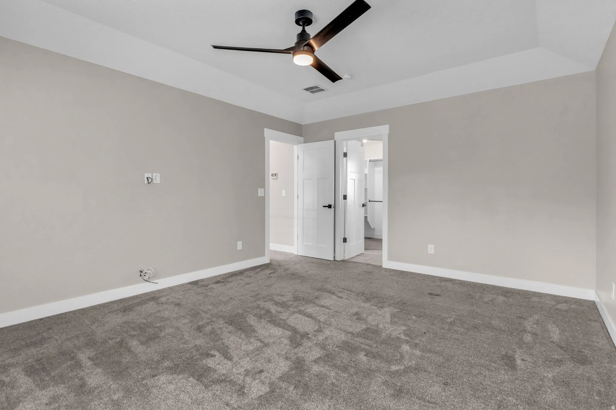 Spacious room featuring neutral paint, gray carpeting, a tray ceiling, and a modern ceiling fan