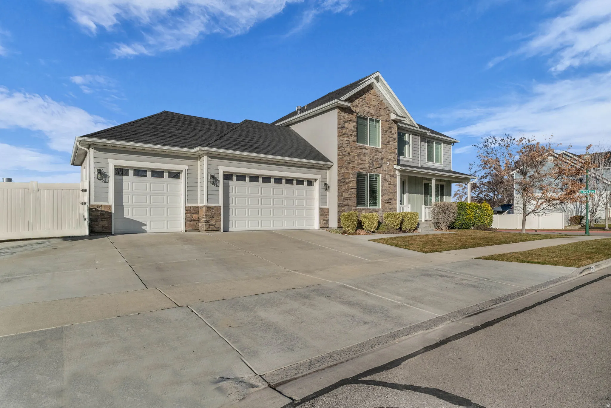 Two-story residence featuring light gray siding, stone veneer accents, an attached three-car garage, and a covered front porch