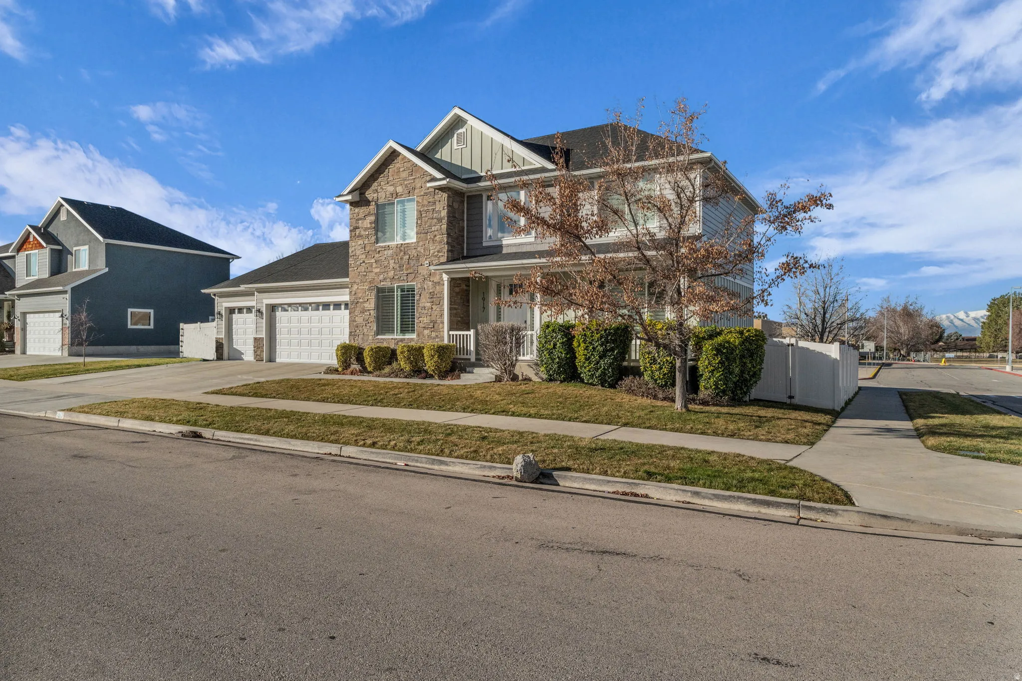 Two-story residence featuring stone and siding facade, a covered front porch, and an attached three-car garage