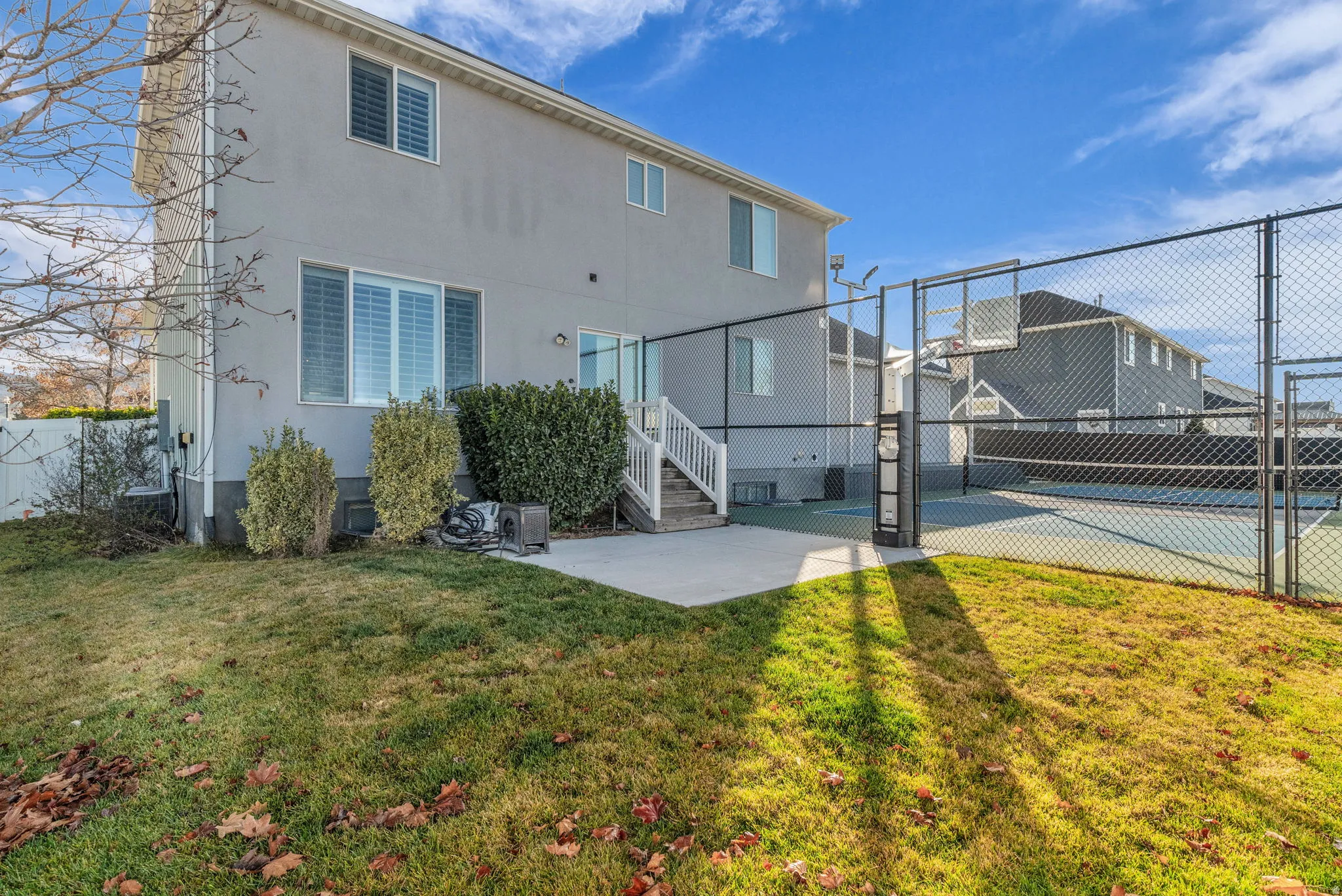 Rear exterior with a concrete patio, white railing, and an adjacent multi-sport court featuring a chain-link fence
