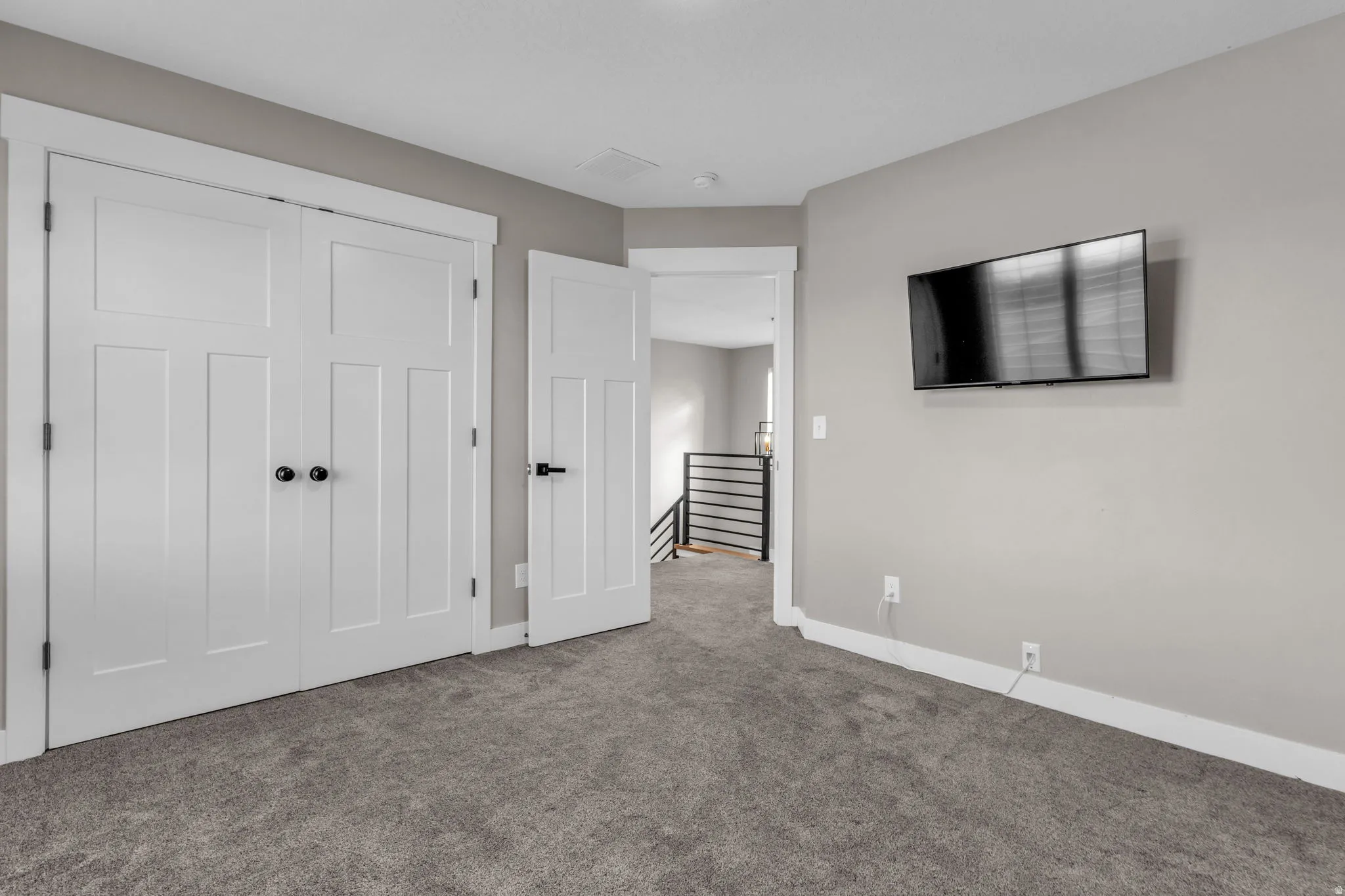 Gray-toned carpeted room featuring white paneled doors with black hardware, neutral wall paint, and white trim