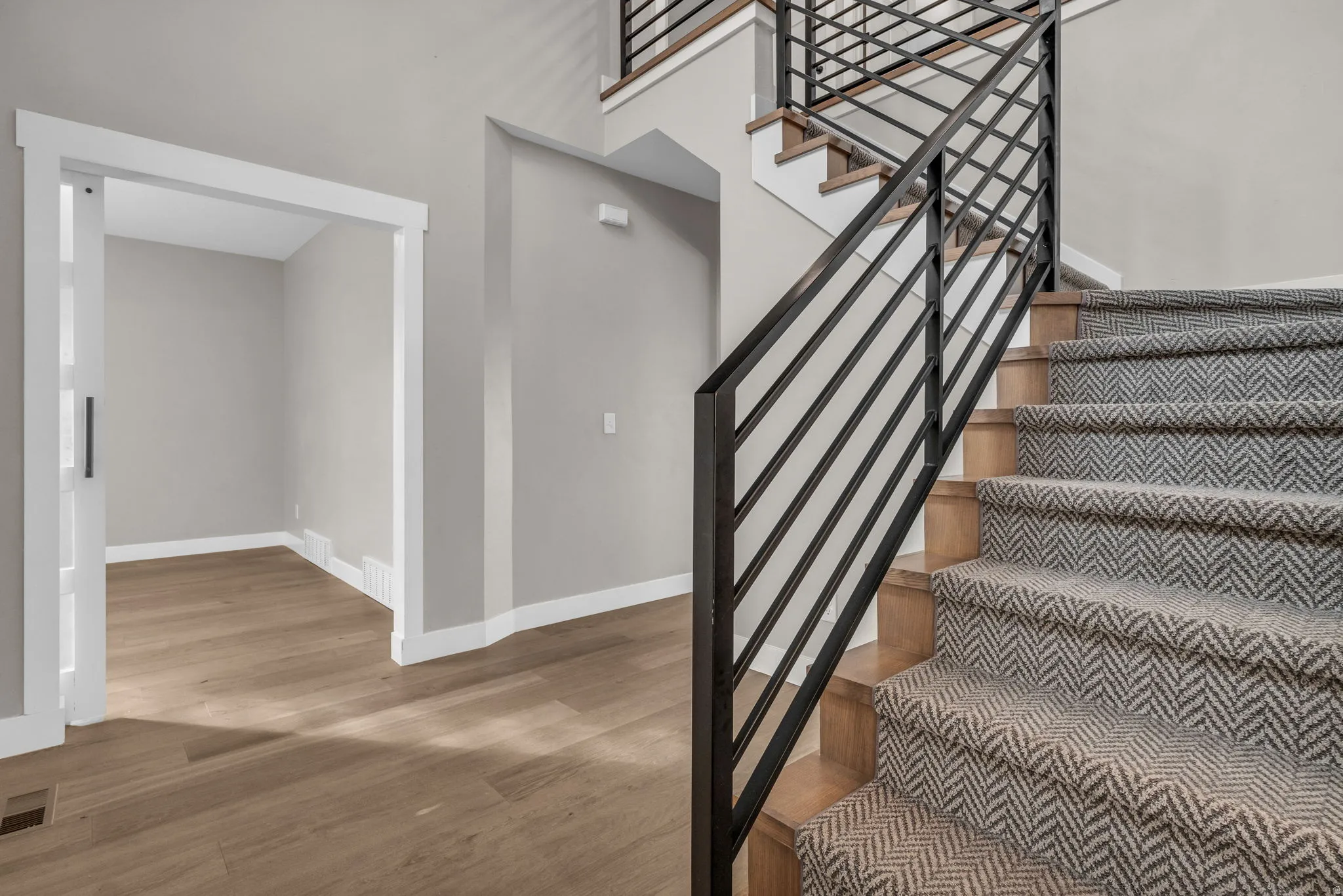 Staircase with wood-finish treads, herringbone-patterned carpet runner, and contemporary black metal railings