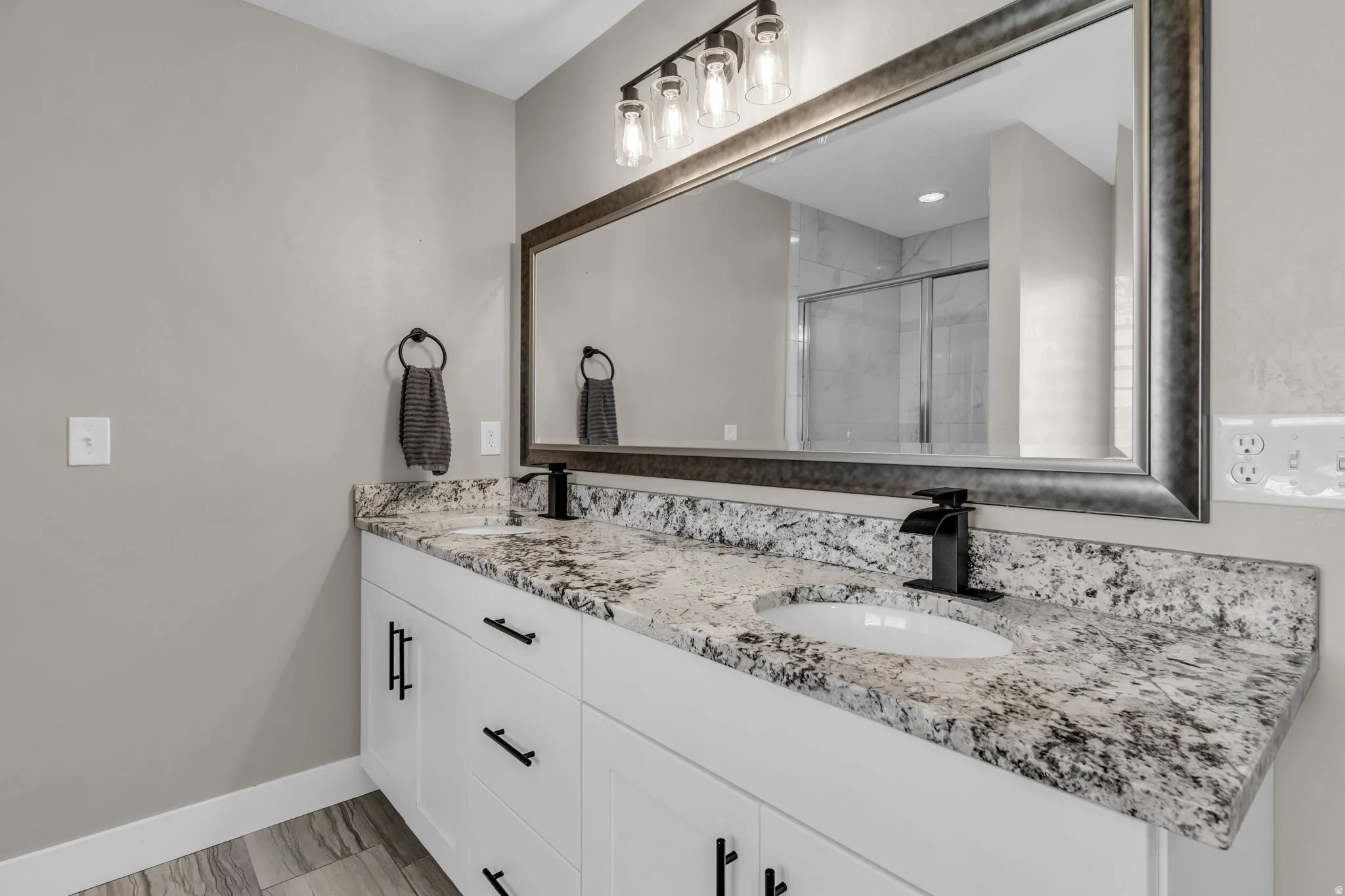 Double vanity with white cabinetry, a speckled countertop, and black waterfall faucets