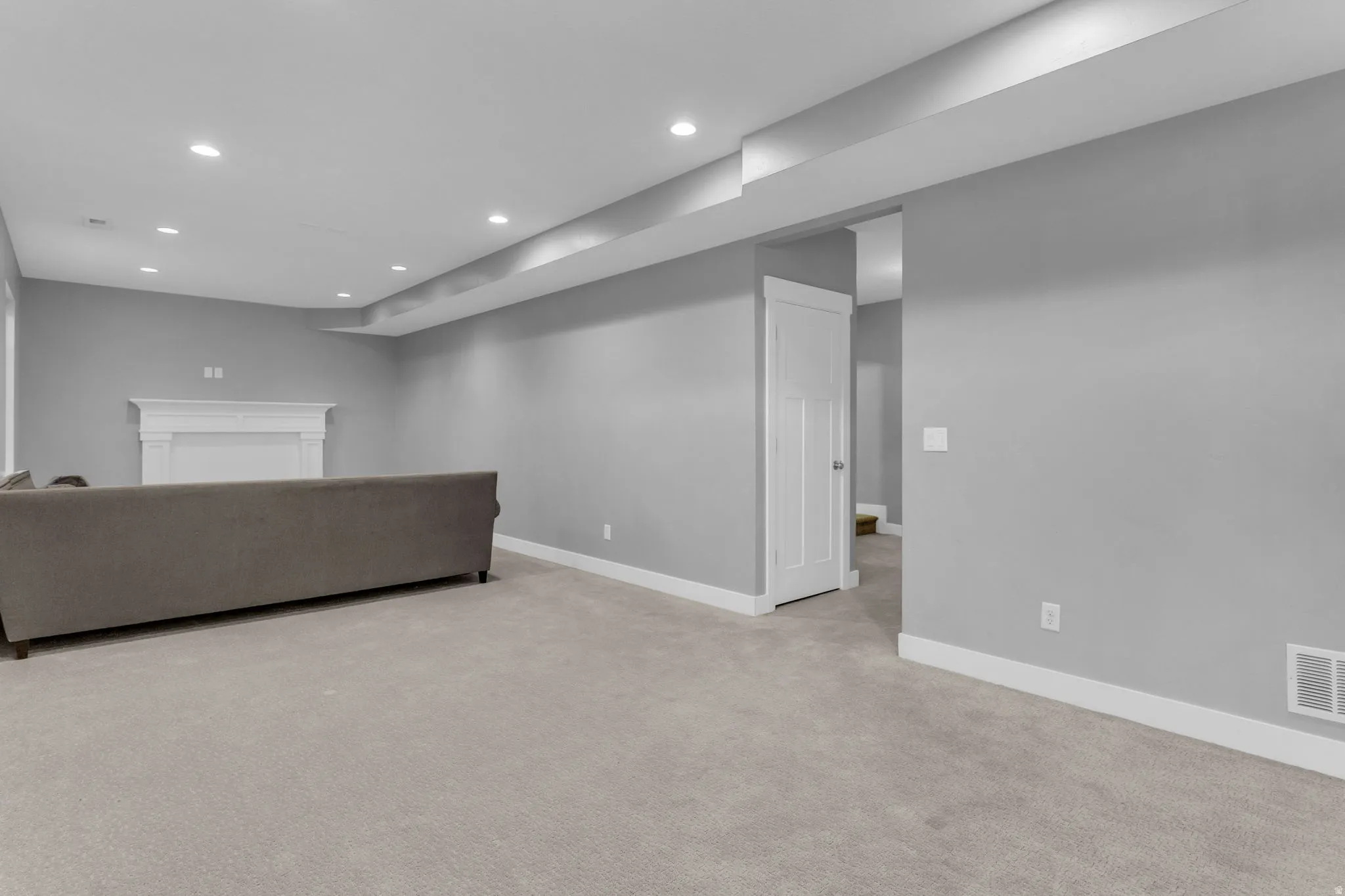 Spacious room featuring light gray walls, recessed lighting, white baseboards, and a white interior door