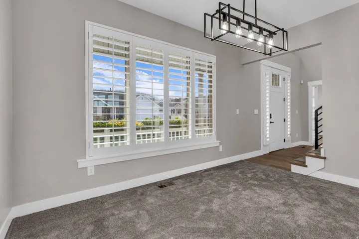 Window with white plantation shutters, gray carpeting, neutral wall paint, and a modern rectangular chandelier