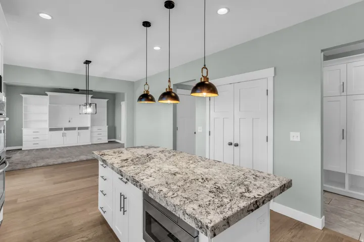 Kitchen island featuring a substantial stone countertop, integrated microwave, and pendant lighting