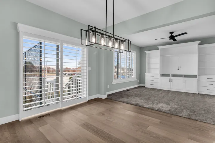 Spacious room featuring wood-finish flooring, a contemporary linear chandelier, and sliding glass doors with plantation shutters