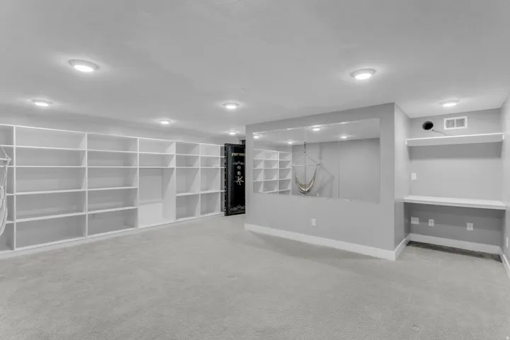 Spacious room featuring extensive built-in shelving, recessed ceiling lighting, light gray carpeting, and a built-in desk area with shelving