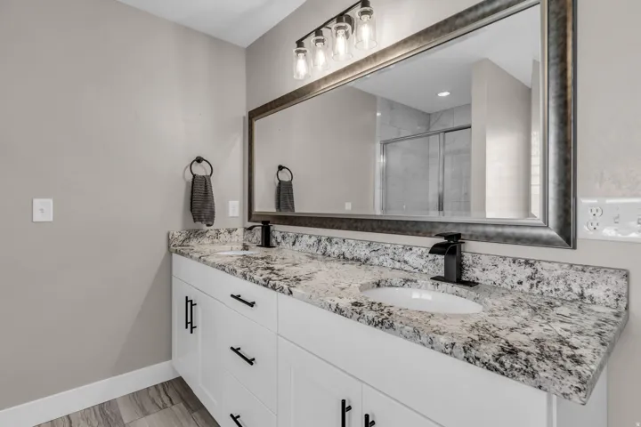 Double vanity with white cabinetry, a speckled countertop, and black waterfall faucets
