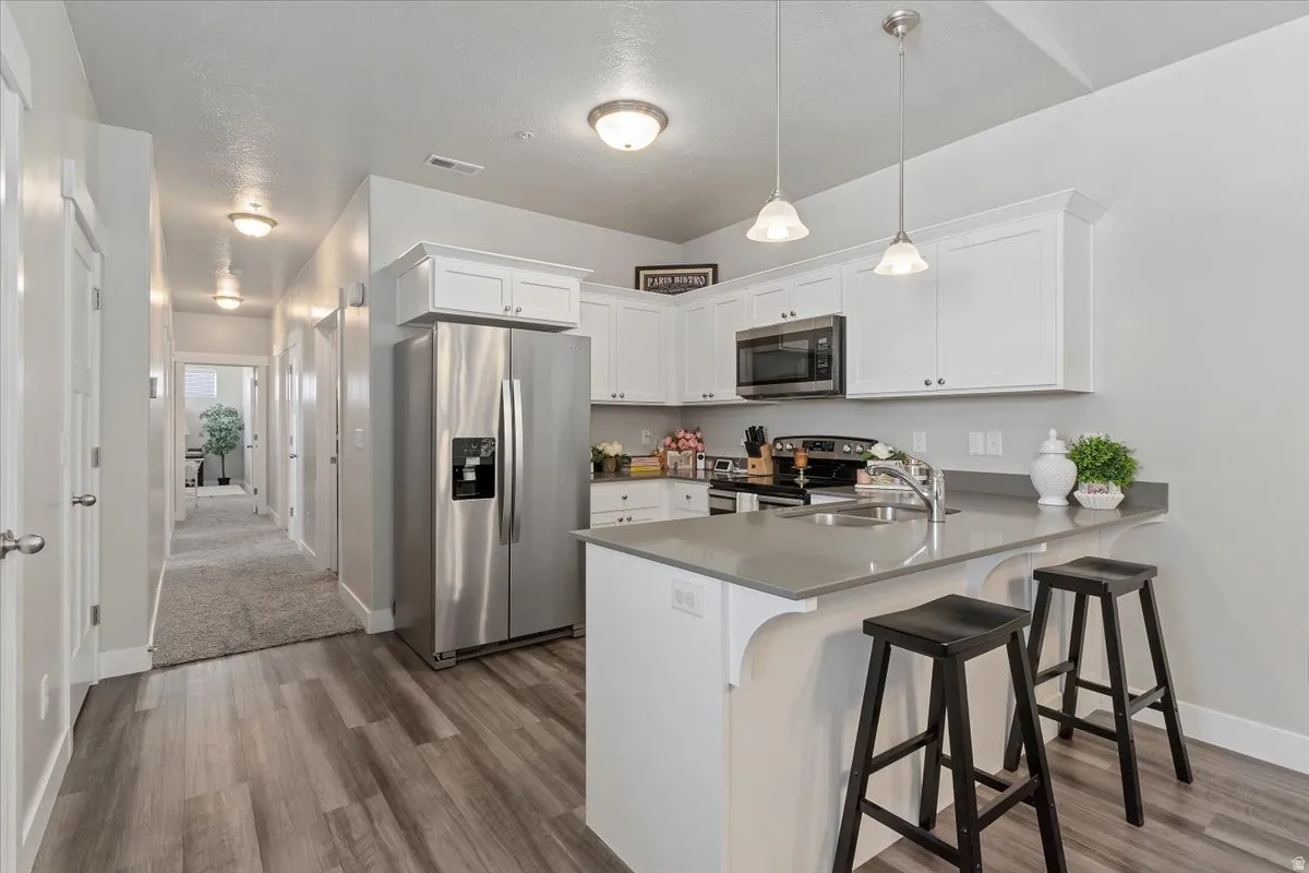Kitchen featuring white cabinetry, stainless steel appliances, a breakfast bar, and pendant lighting