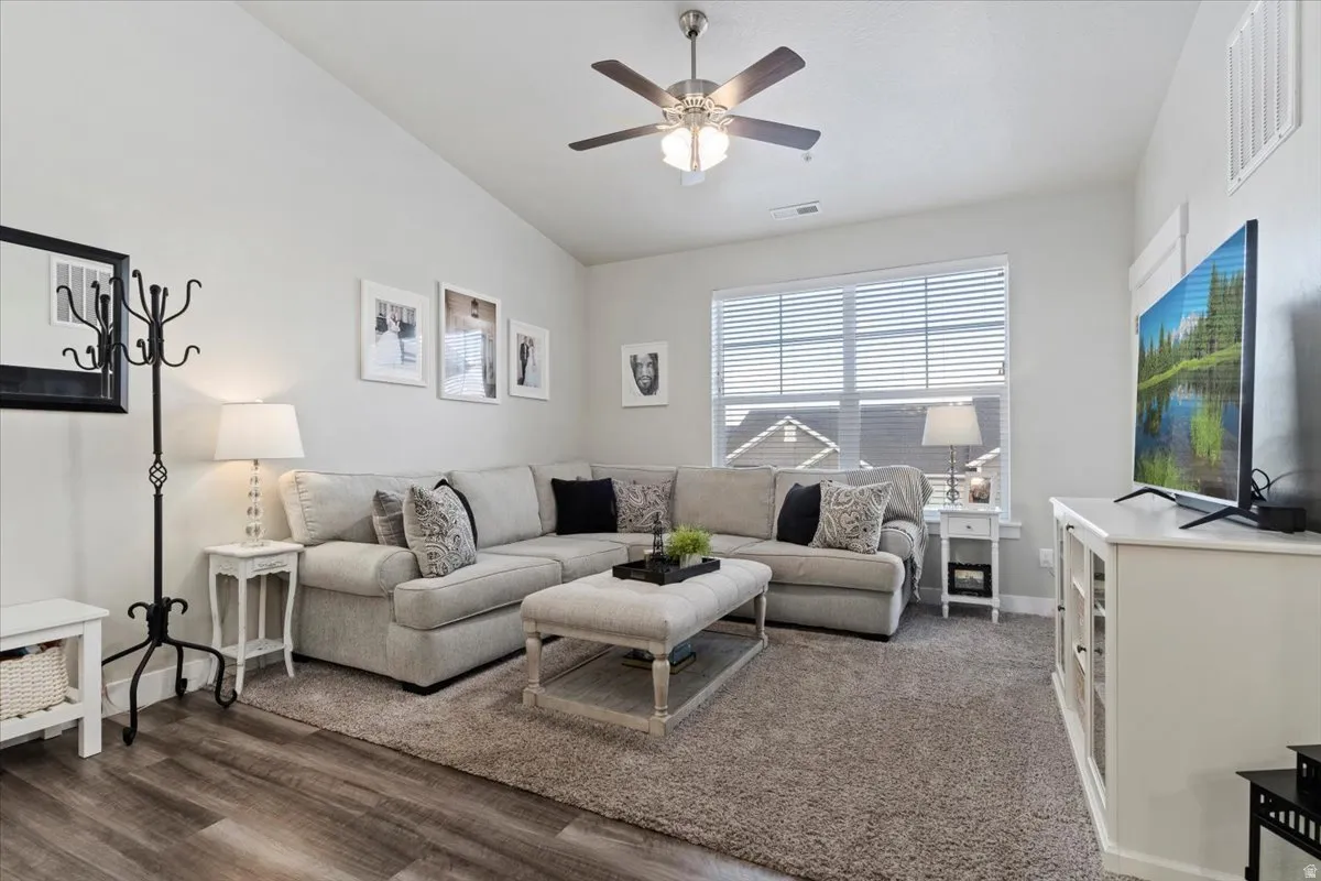 Living area featuring vaulted ceilings, wood-finish flooring, and a ceiling fan with integrated lighting