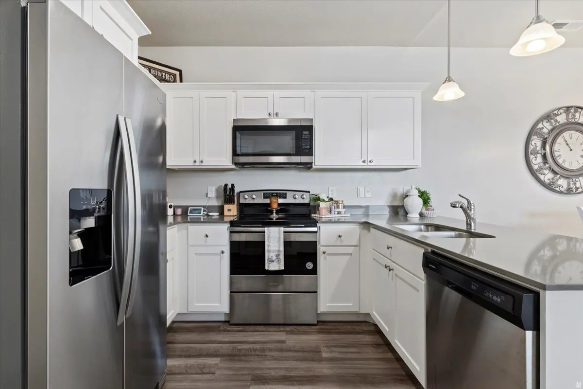 Modern kitchen featuring wood-finish flooring, white cabinetry, stainless steel appliances, and light-toned countertops