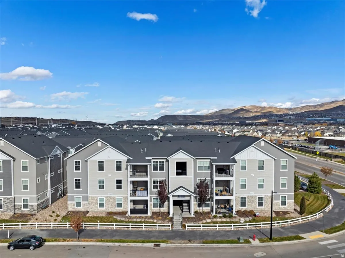 Contemporary apartment building featuring a light gray facade, stone veneer accents, individual balconies, dark gray roofing, and a prominent entry staircase