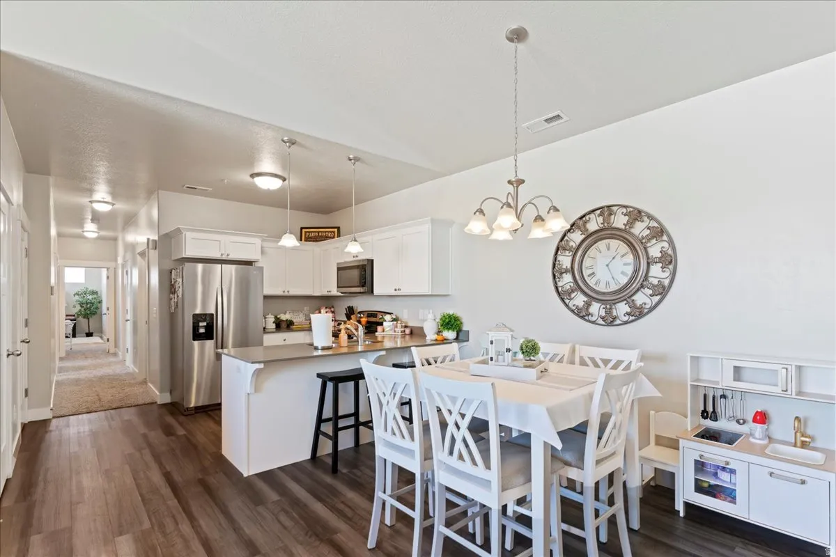 Open-concept kitchen and dining area featuring wood-finish flooring, white cabinetry, stainless steel appliances, and a central island with bar seating