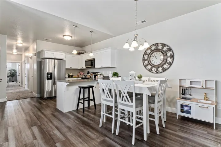 Open-concept kitchen and dining area featuring beautiful lvp flooring, white cabinetry, quartz counters, a kitchen island with counter seating, and stainless steel appliances
