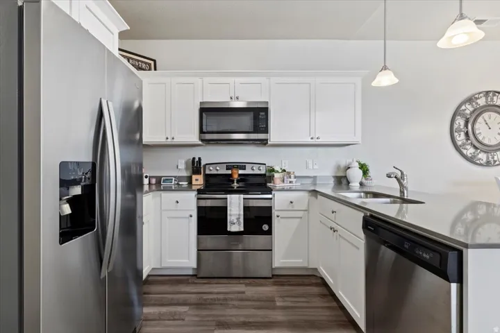 Modern kitchen featuring wood-finish flooring, white cabinetry, stainless steel appliances, and light-toned countertops