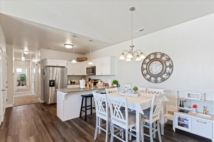 Open-concept kitchen and dining area featuring wood-finish flooring, white cabinetry, stainless steel appliances, and a central island with bar seating