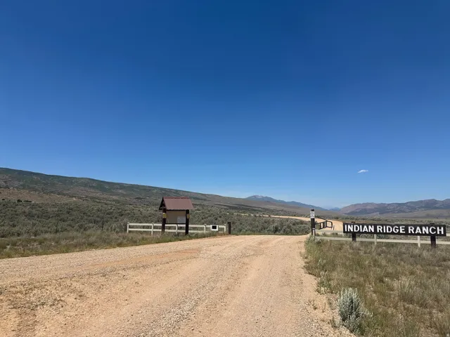 Unpaved road entrance featuring a white wooden fence and a prominent "INDIAN RIDGE RANCH" sign