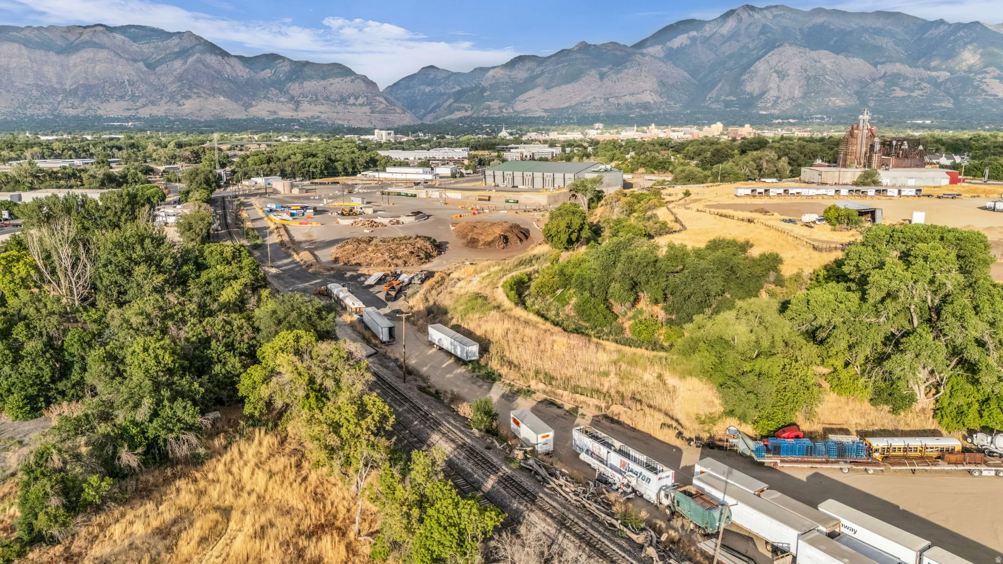 Expansive industrial land featuring a large open lot and perimeter foliage, with visible railroad tracks and commercial vehicles