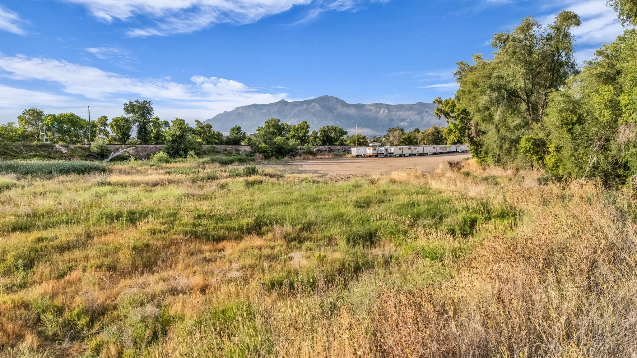 Expansive open field with natural vegetation, framed by distant mountains and a clear sky