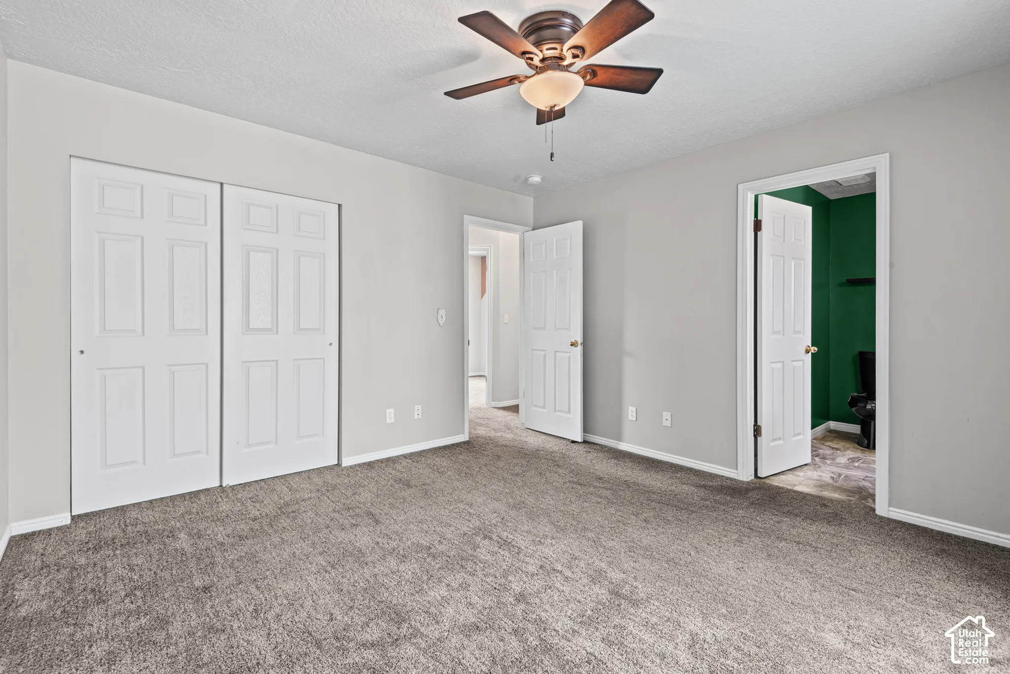 Neutral tone walls, ceiling fan with light fixture, textured carpet, and panel doors
