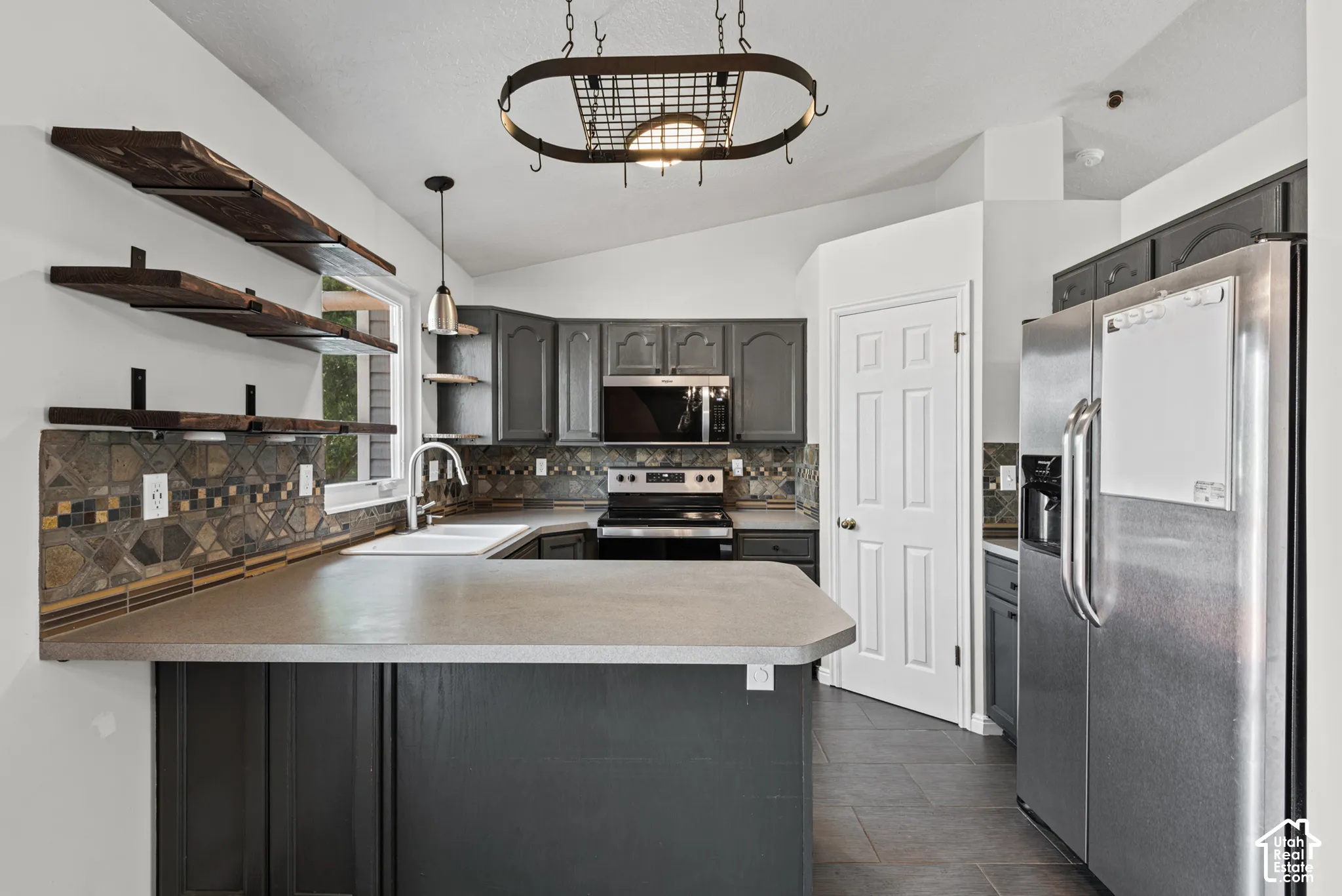 Kitchen featuring dark cabinetry, light-toned countertops, a full suite of stainless steel appliances, and a tiled backsplash