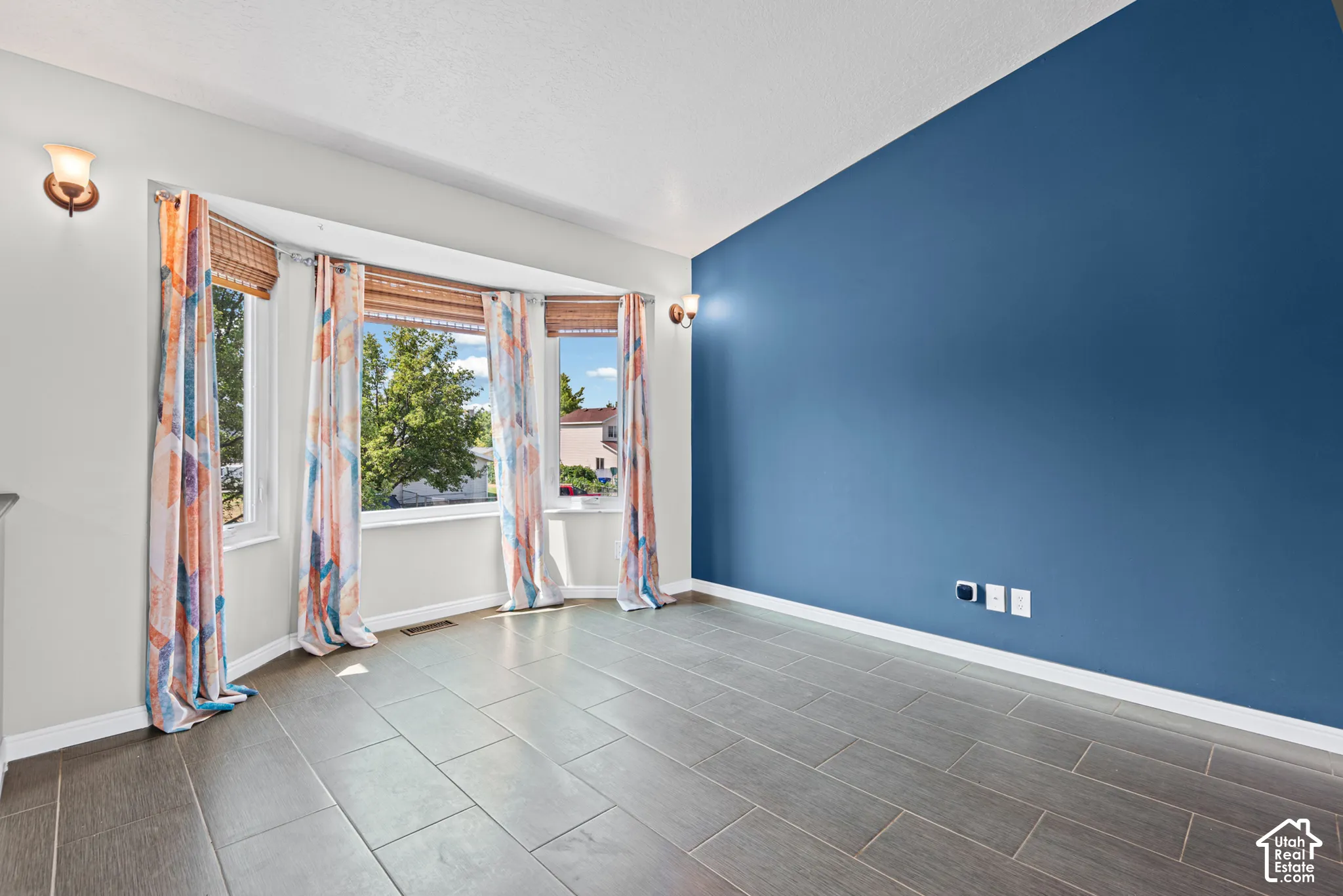 Bright corner bedroom featuring expansive windows with natural light, deep blue accent wall, and herringbone-pattern tile flooring